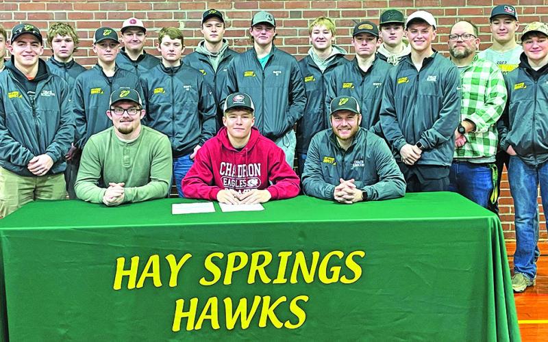 Photo by Jessica Minkten Hay Springs senior Gage Mintken (center) signs his National Letter of Intent with Chadron State College on Wednesday, February 7. Mintken was joined by his Hawks teammates and coaches, along with family and friends, for the event.