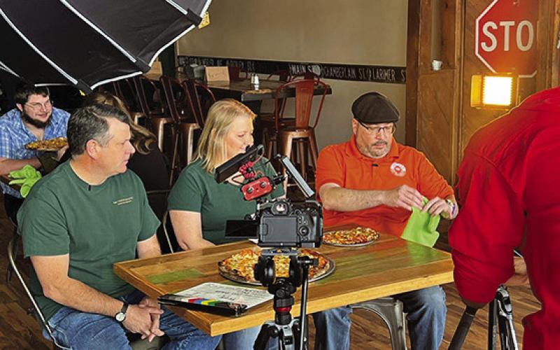 Photo by Shontell Roseberry DeAngelo, from America’s Best Restaurants, films while Courtney and Tosha Fuller watch Luis try some of their pizza at the Twisted Turtle Pub in Rushville, Neb.