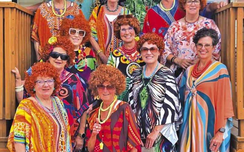 (Courtesy Photo) The fourteen women who participated in the Mrs. Roper Romp stop for a colorful photo on the steps of Sand Ridge Golf Course. On June 20, these ladies put on their brightly colored caftans and red wigs to celebrate the iconic woman Mrs. Roper from the cast of Three’s Company.