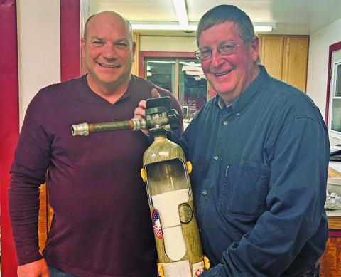 Courtesy Photo Rushville Fire Chief Keith Wellnitz (left) presents an interesting way to store your toilet paper to Jerry Kearns (right) in recognition of his 35 years of service to the Fire Department.