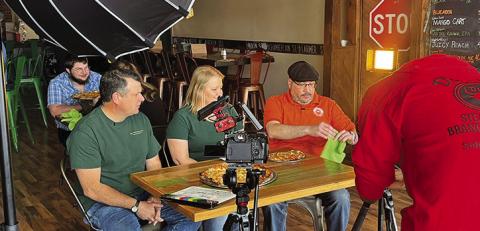 Photo by Shontell Roseberry DeAngelo, from America’s Best Restaurants, films while Courtney and Tosha Fuller watch Luis try some of their pizza at the Twisted Turtle Pub in Rushville, Neb.