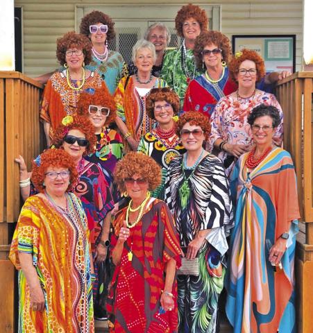 (Courtesy Photo) The fourteen women who participated in the Mrs. Roper Romp stop for a colorful photo on the steps of Sand Ridge Golf Course. On June 20, these ladies put on their brightly colored caftans and red wigs to celebrate the iconic woman Mrs. Roper from the cast of Three’s Company.